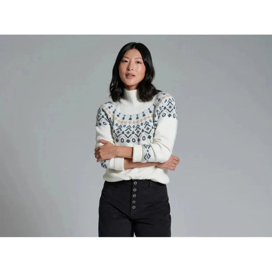 A model wearing the Kuhl Women's Alpina Sweater in Alpine White stands with crossed arms against a gray background.