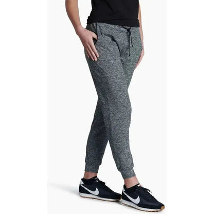 Side view of the Kuhl Women's Bliss Joggr in Dark Heather showing the drawstring waist and cuffed ankles on a model wearing Nike sneakers against a white background.