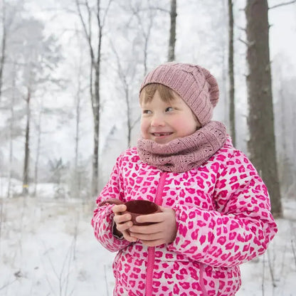 A young girl in a pink leopard print jacket holds a black Kupilka 12 Junior Cup in a snowy forest.