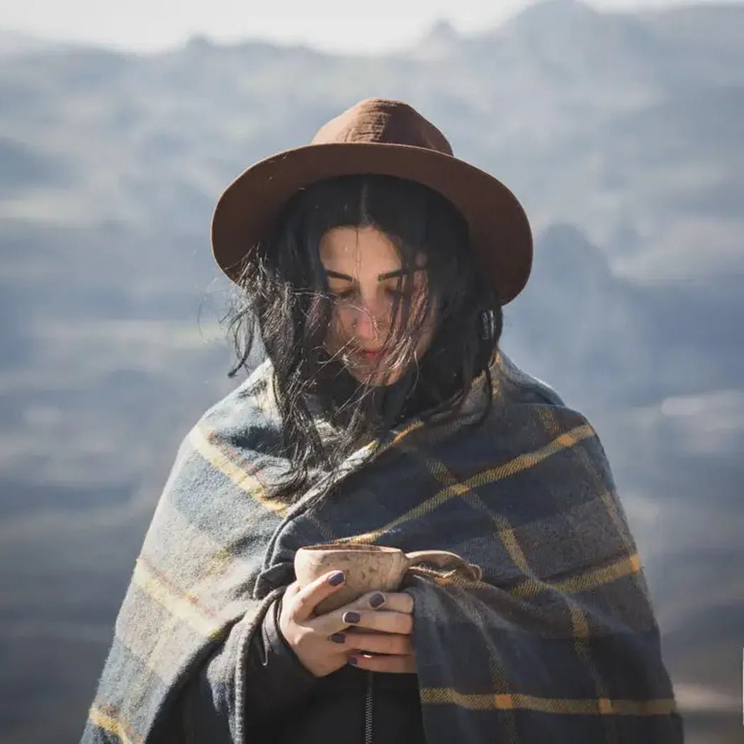 A woman wrapped in a plaid blanket holds the Kupilka 21 Classic Cup, with mountains in the background.