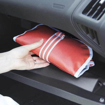 A hand holds the red Kurgo First Aid Kit with white trim in a car's glove compartment.