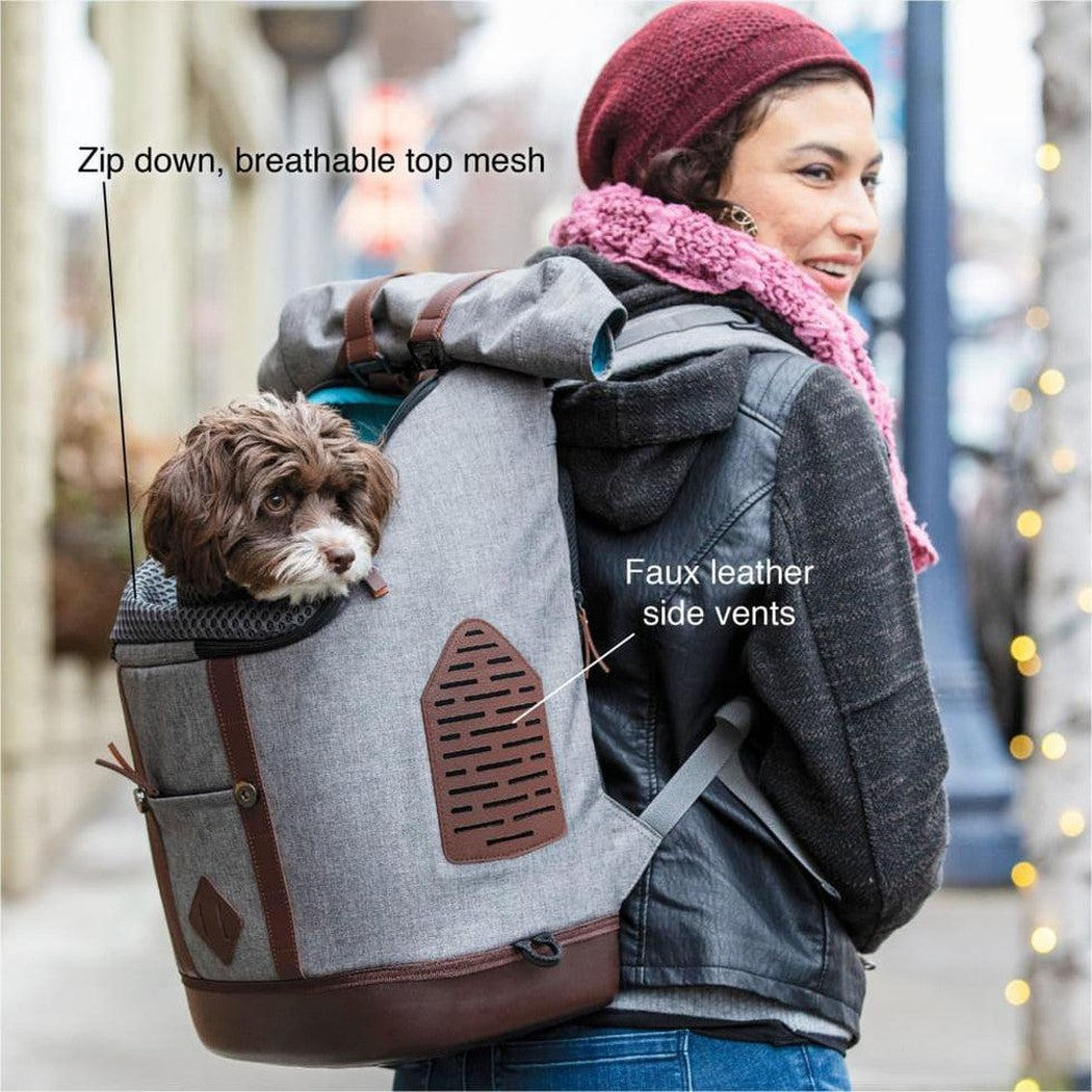 A woman wears the Kurgo K9 Rucksack in Heather Grey with a dog in the front pocket, showing the breathable top mesh and faux leather side vents.