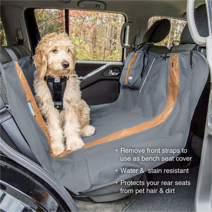 A dog sits on a Charcoal Kurgo Wander Hammock car seat cover with a forest background visible through the window.
