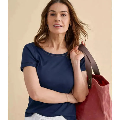 A woman wearing the L.L.Bean Women's Pima Cotton Tee, Short-Sleeve Jewelneck in Raven Blue poses with a red tote bag against a beige background.
