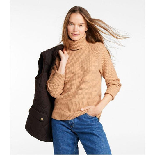 A model wears the L.L.Bean Women's SuperSoft Waffle Turtleneck Sweater in HoneyBrownHeath with blue jeans and a charcoal vest, against a white background.