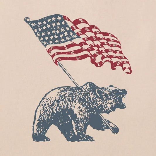 A bear holding an American flag on a Birch White Crusher Tee.