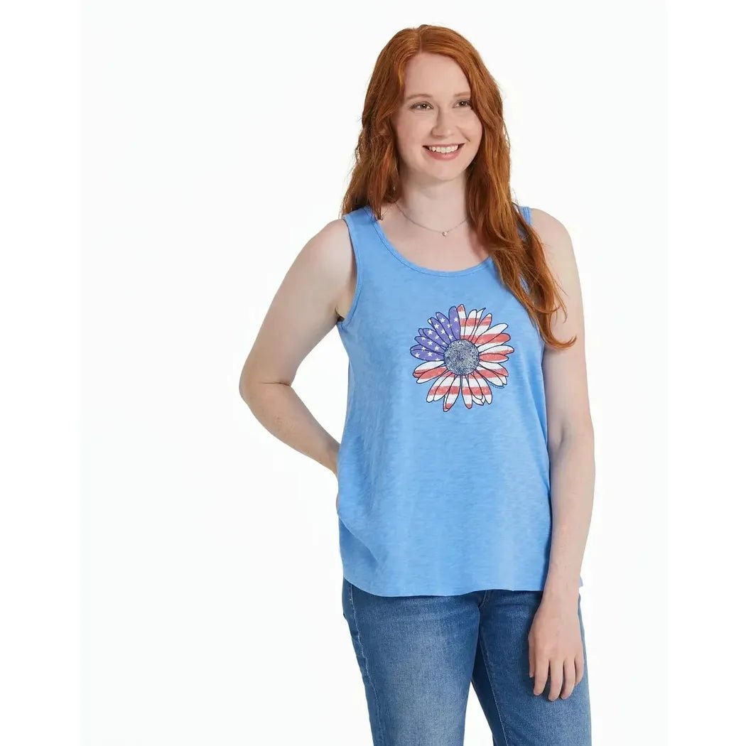 A woman wearing the Life is Good Women's America The Beautiful Daisy Textured Slub Tank in Cornflower Blue stands against a white background.