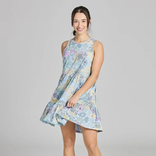 A woman wearing the Life is Good Women's Botanical Garden Pattern Tiered Tank Dress in Glacier Blue stands against a plain gray background.
