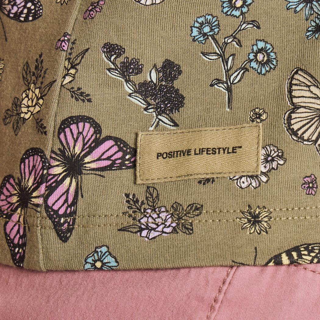 A close-up of the Life is Good Women's Butterfly Garden Pattern Crusher Boxy Tank in Moss Green showing the "Positive Lifestyle" tag and butterfly design.
