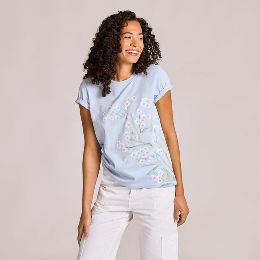 A woman wearing the Life is Good Women's Forgetmenot Butterfly Short Sleeve Crusher Tee in Glacier Blue stands against a light gray background.