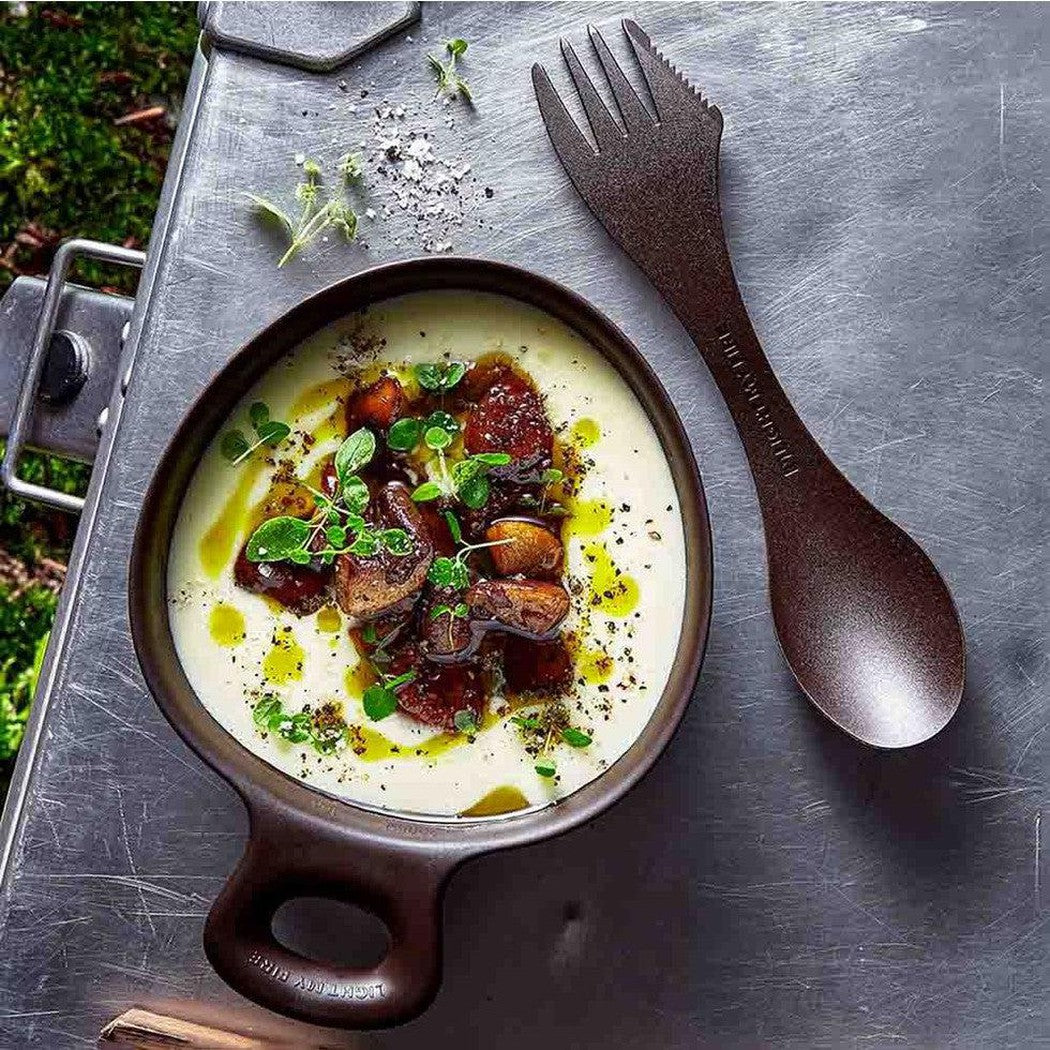A top-down view of the Light My Fire Outdoor MealKit BIO in Hazy Blue showing the dishware and utensil on a metal surface with greenery in the background.