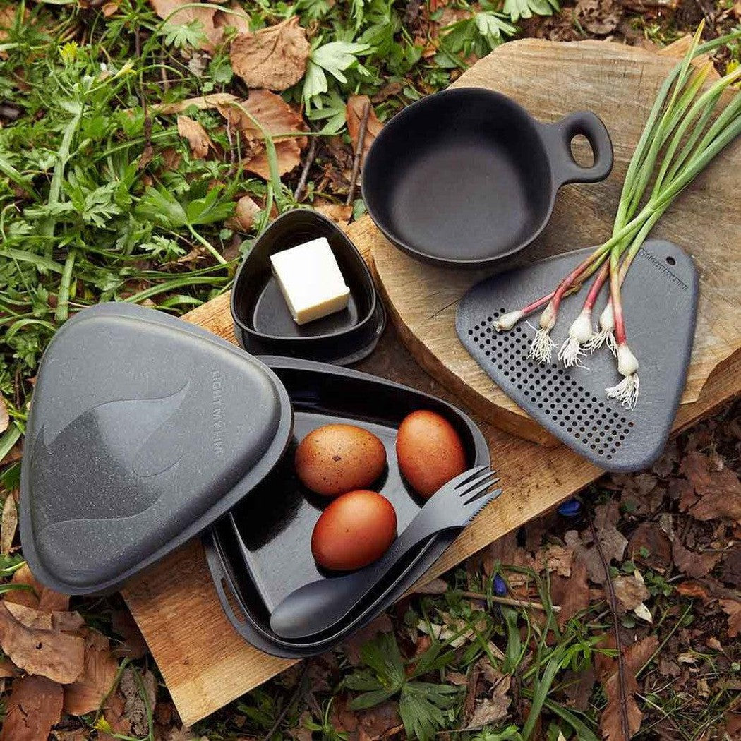 A top-down view of the Light My Fire Outdoor MealKit BIO in Hazy Blue showing eggs and butter on a wooden board with greenery in the background.