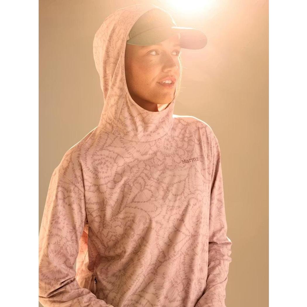 A woman wears the Marmot Women's AirExchange SolarShield Hoody in Dust Twirl, with the hood up and a cap, against a light background.