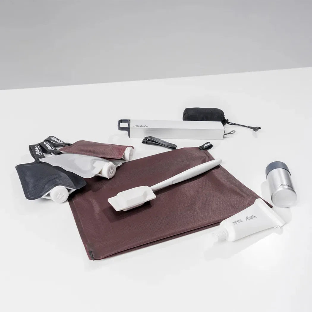 A top-down view of the Matador FlatPak Zipper Toiletry Case in Arctic White on a white surface with toiletries.