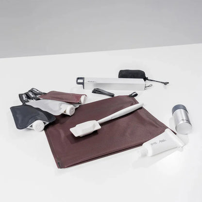 A top-down view of the Matador FlatPak Zipper Toiletry Case in Arctic White on a white surface with toiletries.