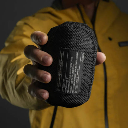A person in a yellow jacket holds the black Matador Freefly 16 Packable Backpack toward the camera.