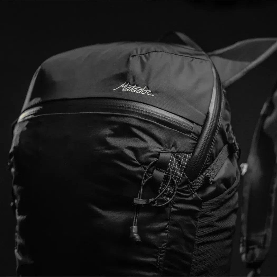 A close-up of the Matador Freefly 16 Packable Backpack in Black, showing the front zipper and logo against a dark background.