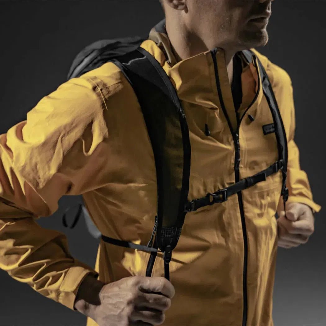 A man wears the black Matador Freefly 16 Packable Backpack, showing the shoulder straps and chest harness against a dark background.