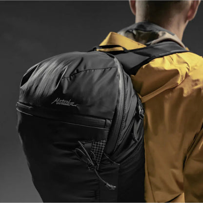 Back view of the Matador Freefly 16 Packable Backpack in Black on a model wearing a yellow jacket against a dark background.