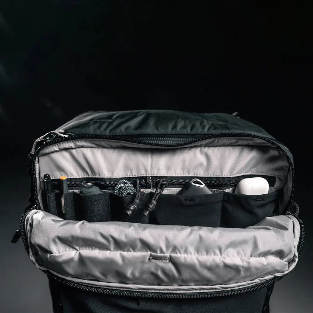 Back view of the Matador Globerider 45 Travel Backpack in Black showing the organized front pocket with pens and a white mouse against a dark background.