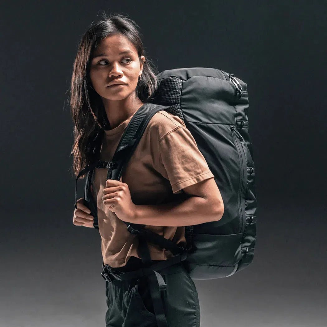 A woman wearing the Matador SEG 45 Travel Pack in Black stands against a dark background.