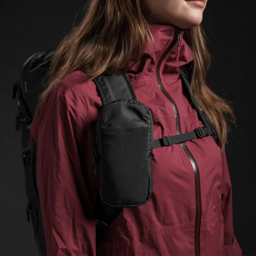A woman in a maroon jacket wears the black Matador Speed Stash on her chest strap, with a backpack visible behind her.