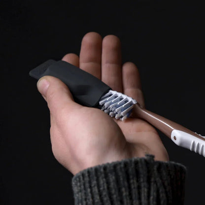 A hand holds a black Matador Toothbrush Cap with a rose gold toothbrush, against a dark background.