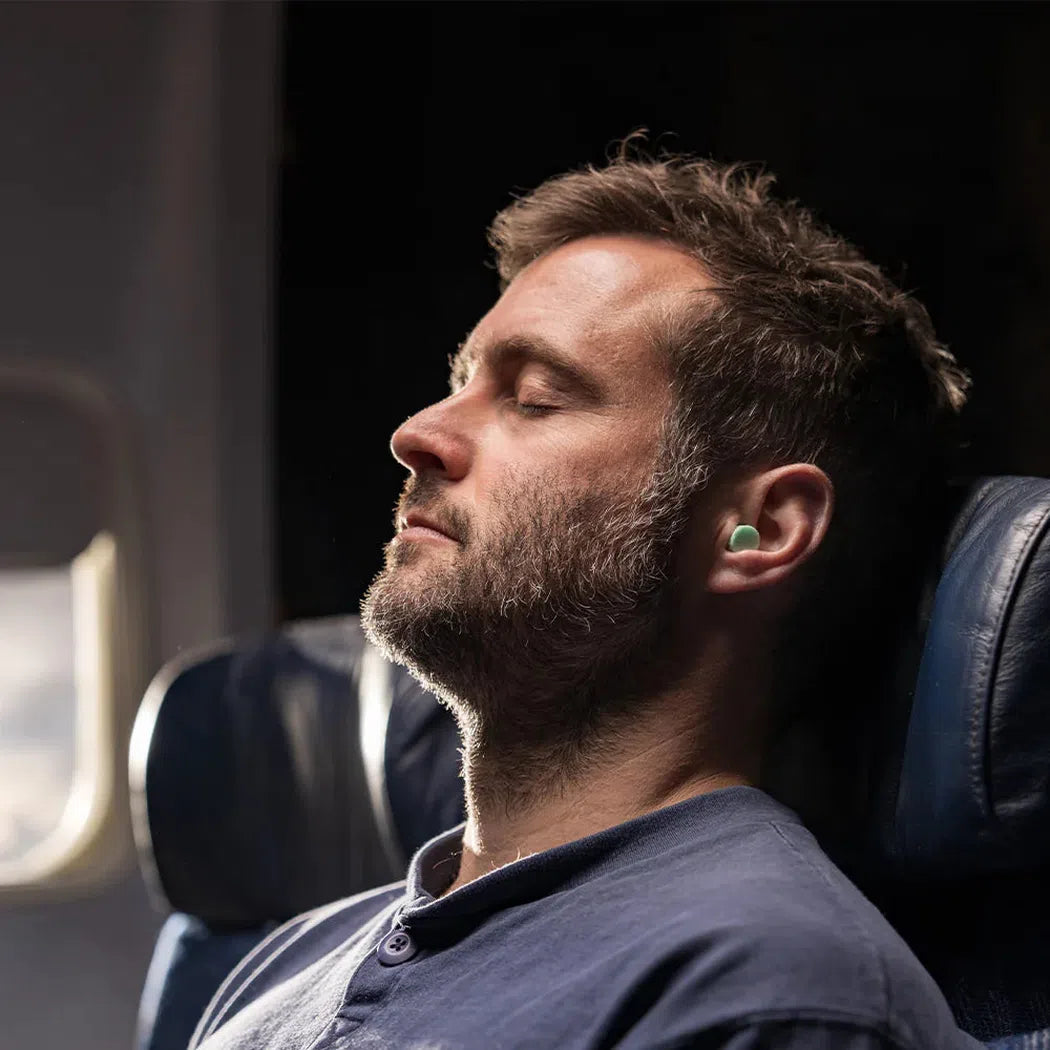 A man sleeping on an airplane wearing the Matador Travel Earplugs Kit in his ear.