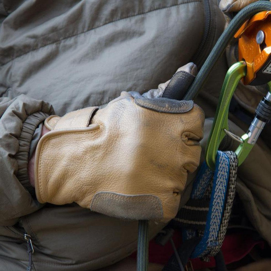 A close-up of a person wearing a Natural Metolius Belay Glove - Full Finger with a green carabiner attached, against a charcoal-colored jacket.