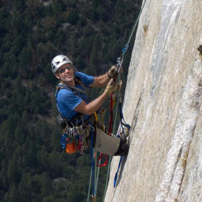 A climber wearing Metolius Climbing Glove - 3/4 Finger gloves scales a rock face with trees in the background.