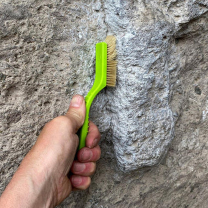 A hand holds the Metolius Razorback Boar's Hair Brush against a gray rock face.