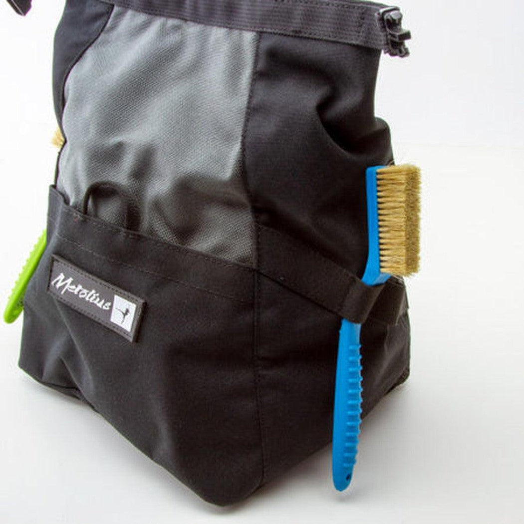 A blue Metolius Razorback Boar's Hair Brush hangs from the side of a black and gray Metolius bag against a white background.