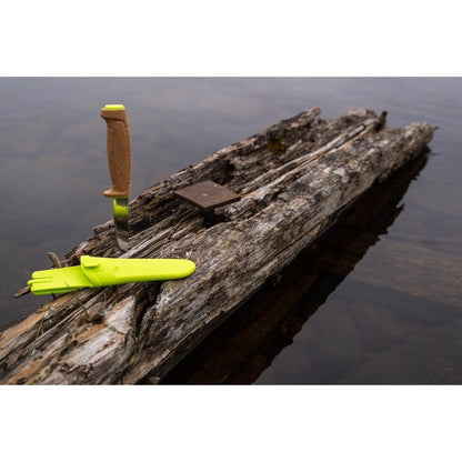 A Morakniv Floating Knife in Lime Green rests on a weathered log floating in calm water.
