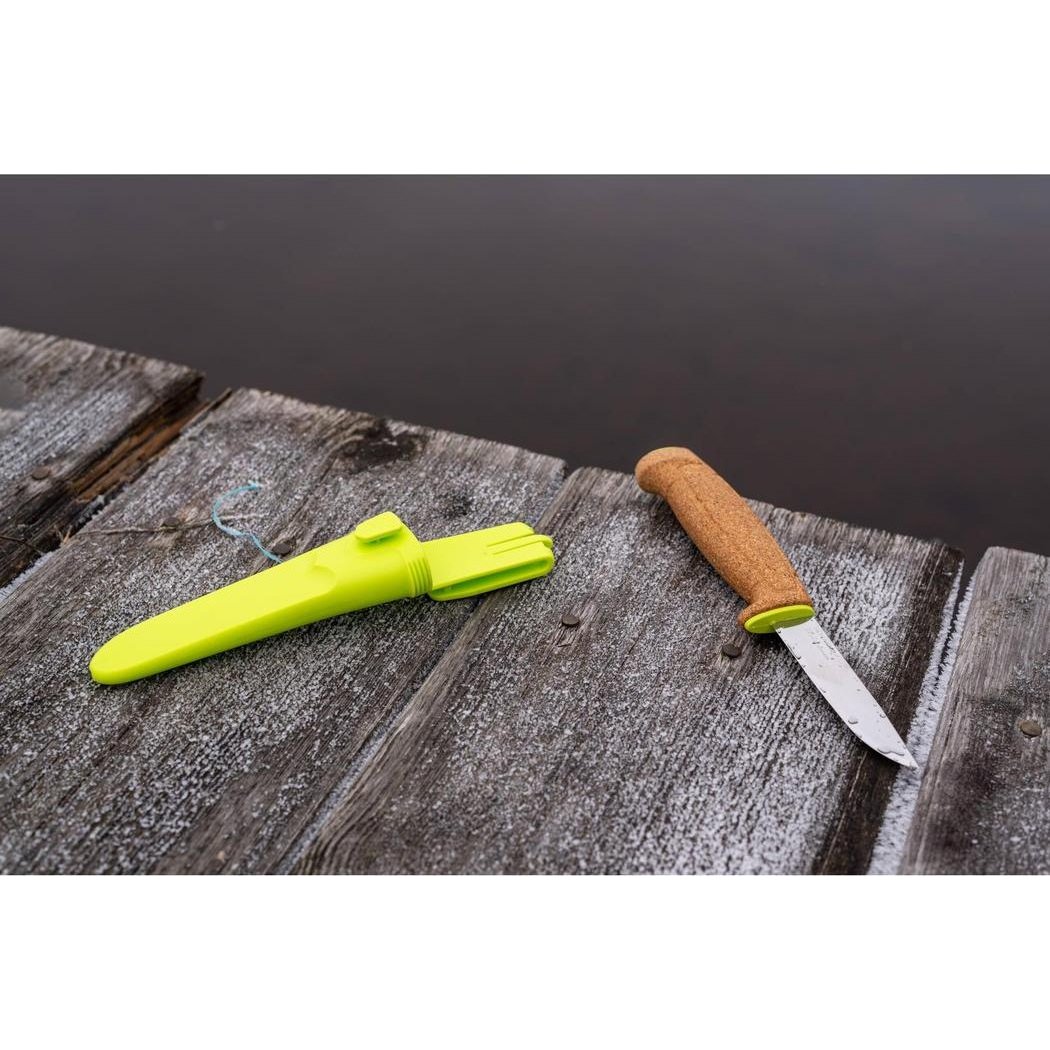 A lime green Morakniv Floating Knife and its sheath rest on a weathered wooden dock by the water.
