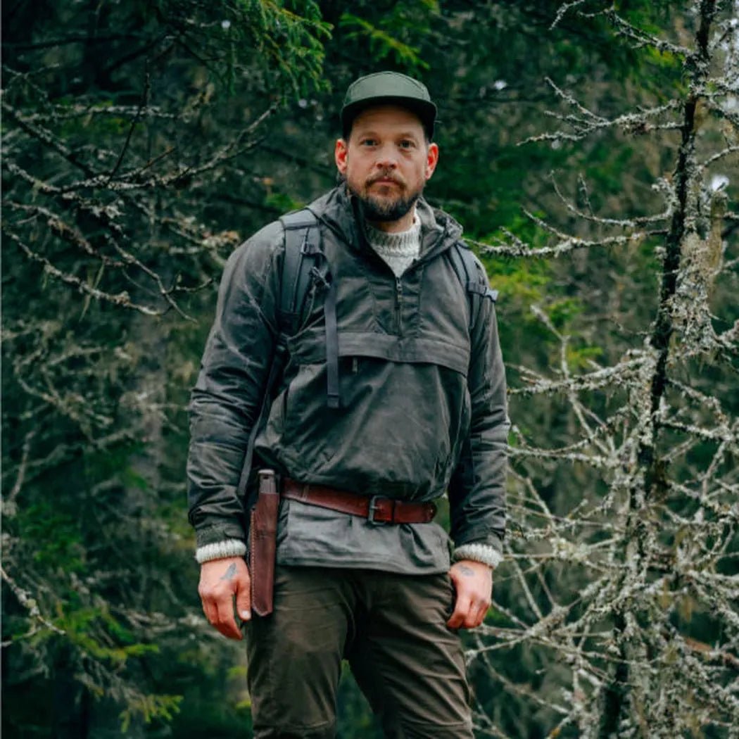 A man stands in a forest wearing the Morakniv Garberg Grand (Stainless) knife in Black, with a brown leather sheath visible on his hip.