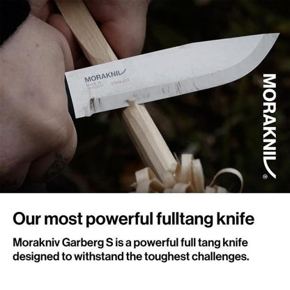 A hand holds the Morakniv Garberg Stainless Steel Knife with a wooden handle, showing the blade cutting wood shavings in a close-up shot.