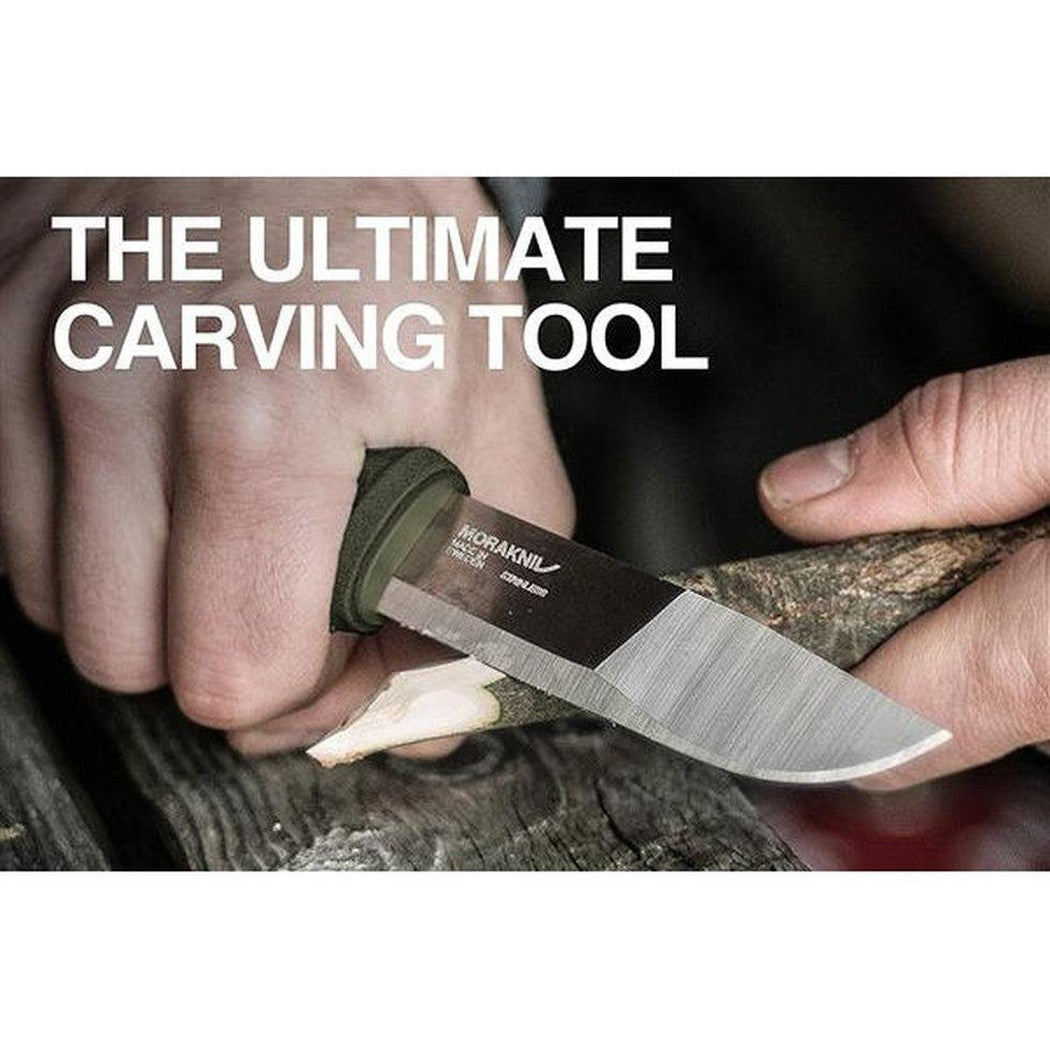 A hand holds the Morakniv Kansbol Knife with a green handle while carving wood.