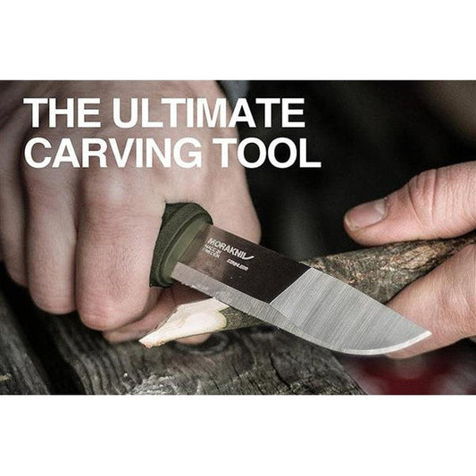 A hand holds the Morakniv Kansbol Knife with a green handle while carving wood.