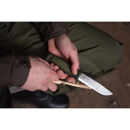A person holding the Morakniv Kansbol Knife in Green, showing the blade and handle against a dark background.
