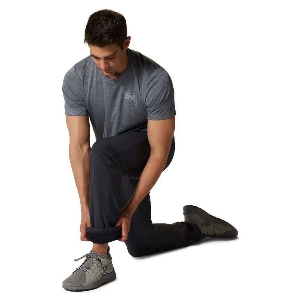 A man kneels on one knee adjusting the cuff of his Mountain Hardwear Men's Yumalino Lined Pant in Dark Storm against a white background.