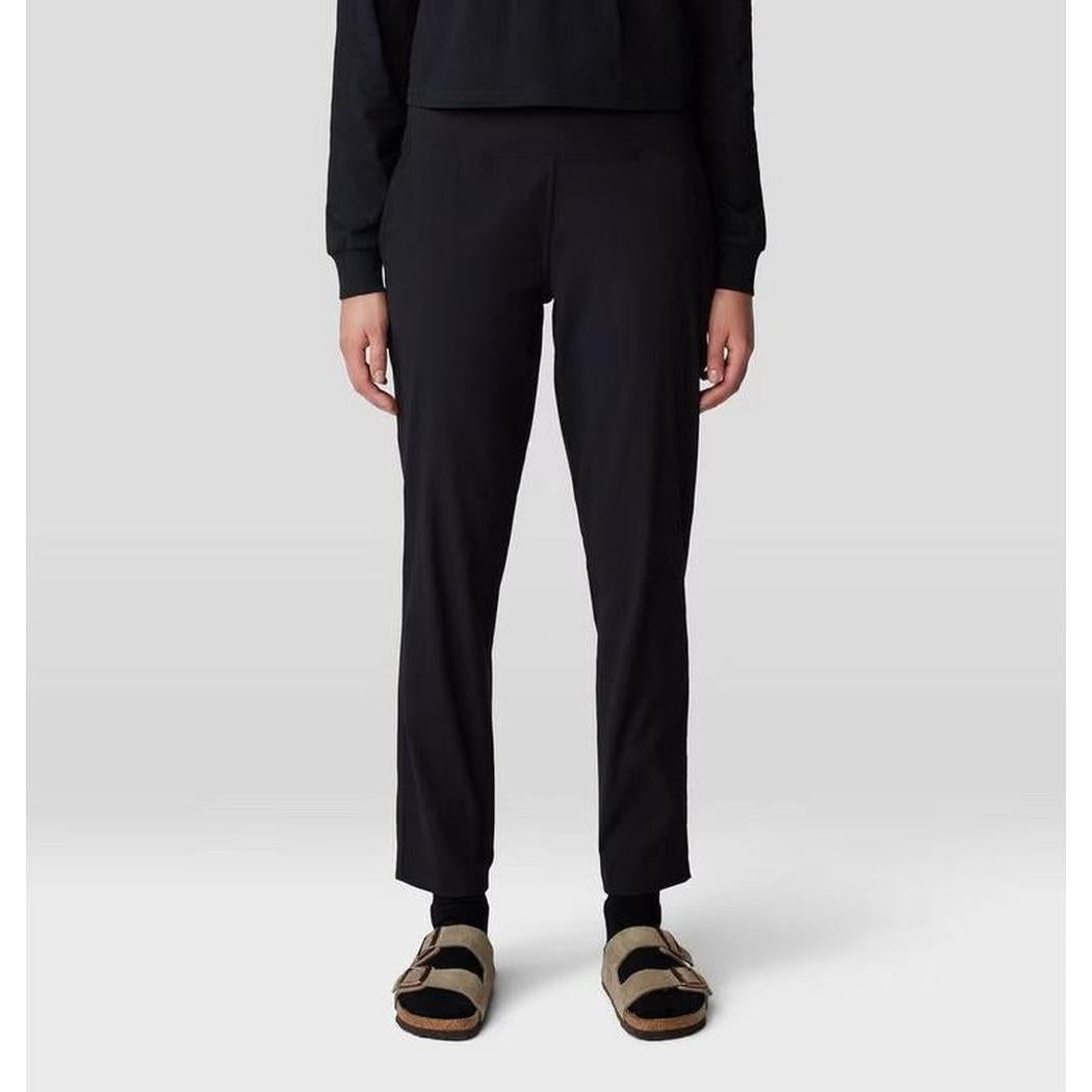 A front view of the Mountain Hardwear Women's Dynama Ankle Pant in Black, showing the model wearing it with black socks and tan sandals against a light gray background.