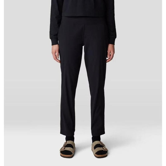 A front view of the Mountain Hardwear Women's Dynama Ankle Pant in Black, showing the model wearing it with black socks and tan sandals against a light gray background.