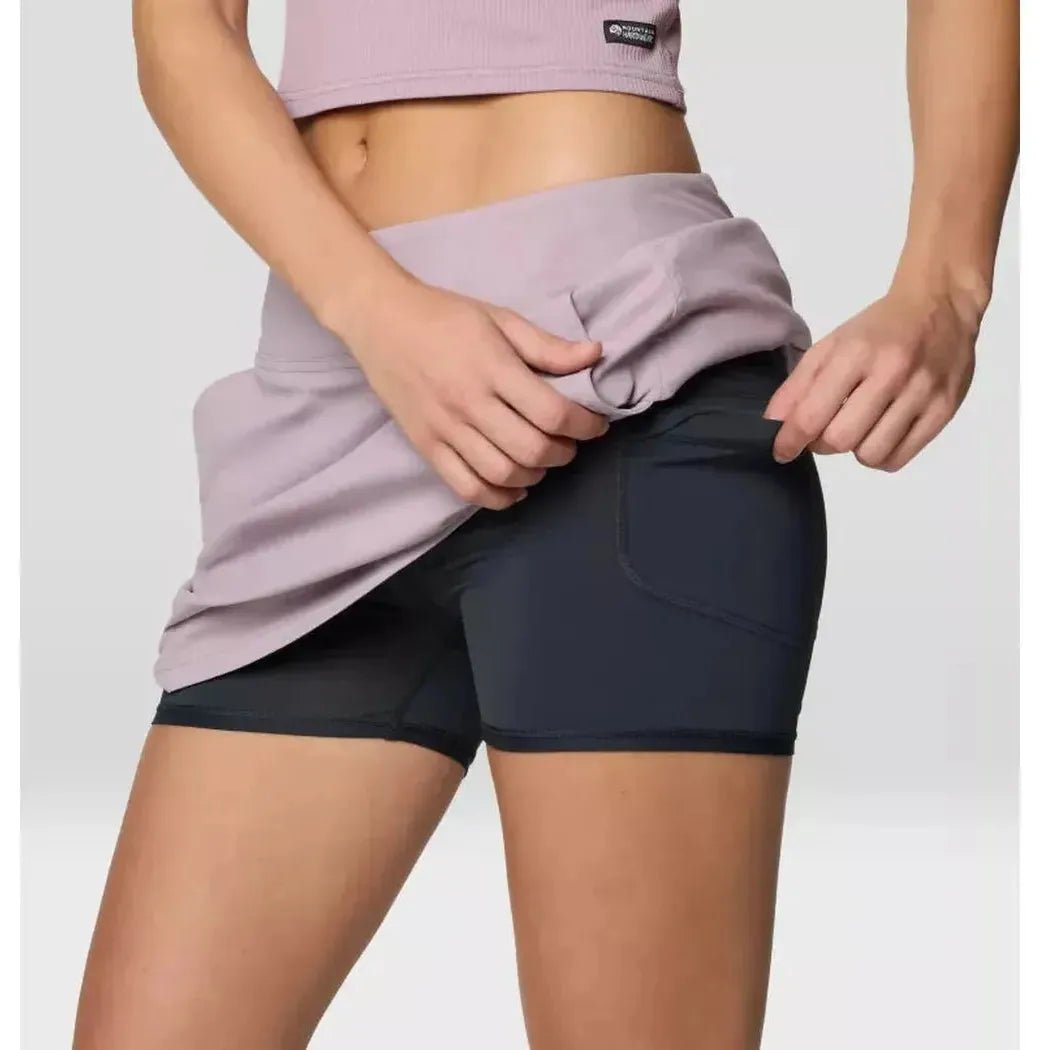 A woman wearing the Mountain Hardwear Women's Dynama Skort in Daze adjusts the waistband against a plain background.