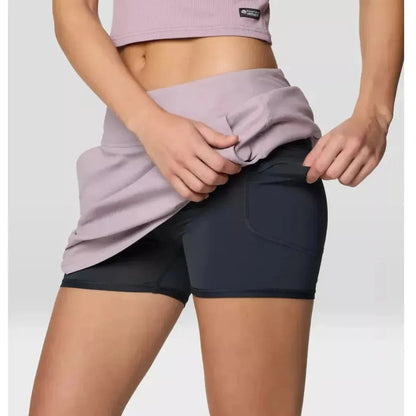 A woman wearing the Mountain Hardwear Women's Dynama Skort in Daze adjusts the waistband against a plain background.