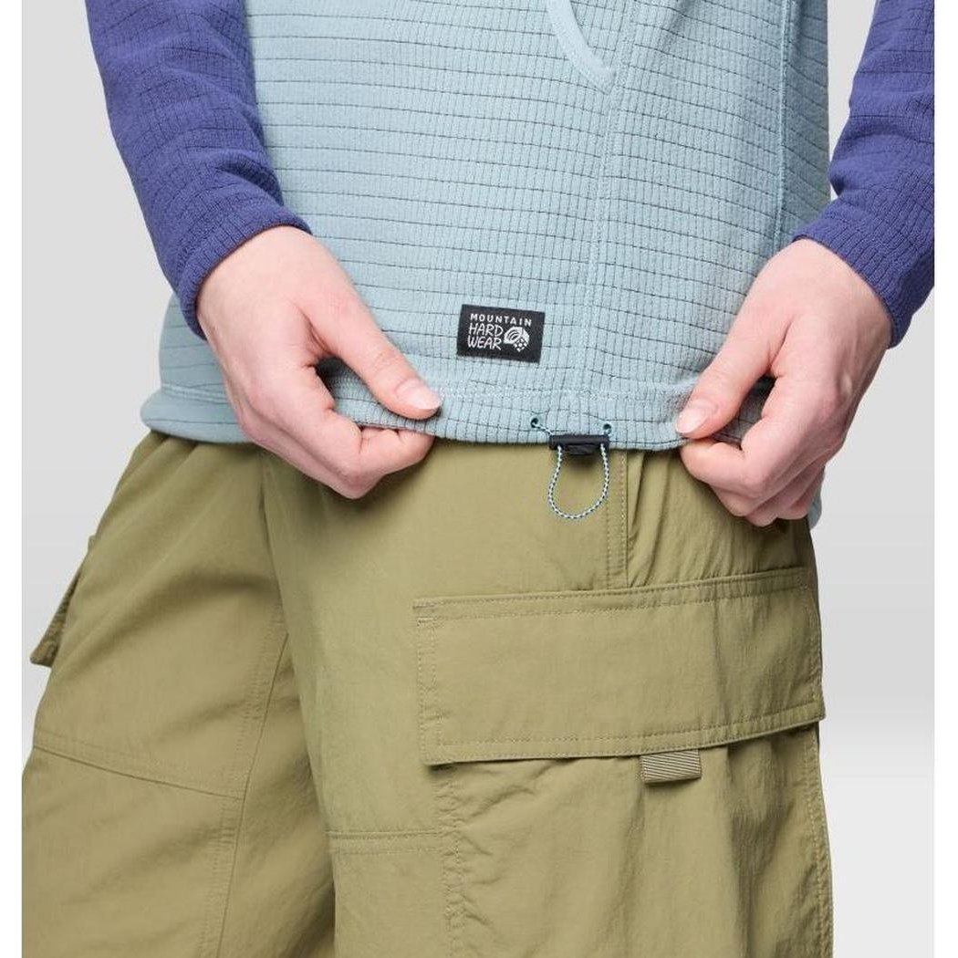 A close-up of the Mountain Hardwear Women's Summit Grid Tunic Hoody in Ice Shadow/Lapis Dusk, showing the model adjusting the waistband with cargo shorts against a plain background.