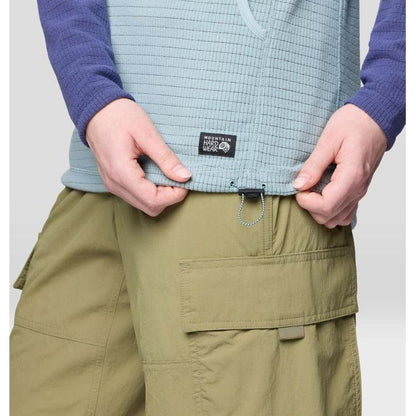 A close-up of the Mountain Hardwear Women's Summit Grid Tunic Hoody in Ice Shadow/Lapis Dusk, showing the model adjusting the waistband with cargo shorts against a plain background.