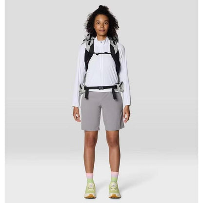 A front view of the Mountain Hardwear Women's Sunshield Half Zip in Fogbank on a model with a backpack and gray shorts against a plain background.