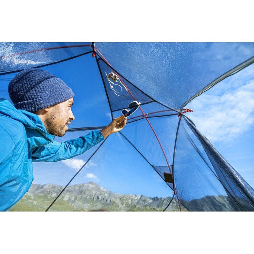 A man in a blue jacket sets up the MSR FreeLite 2 Tent against a mountainous backdrop.