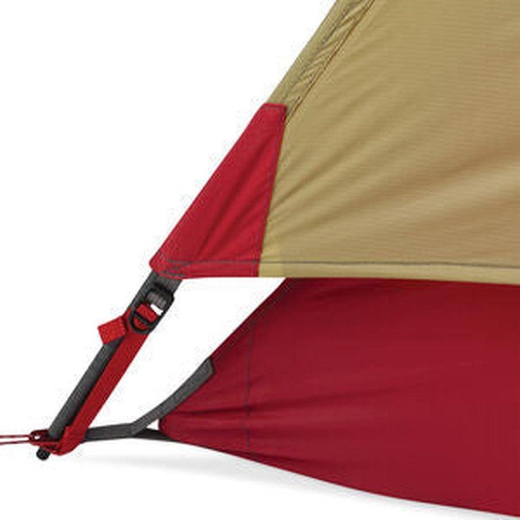 Close-up of the MSR Hubba Hubba 2 Tent V9 showing the red and tan fabric with a red strap and buckle against a white background.