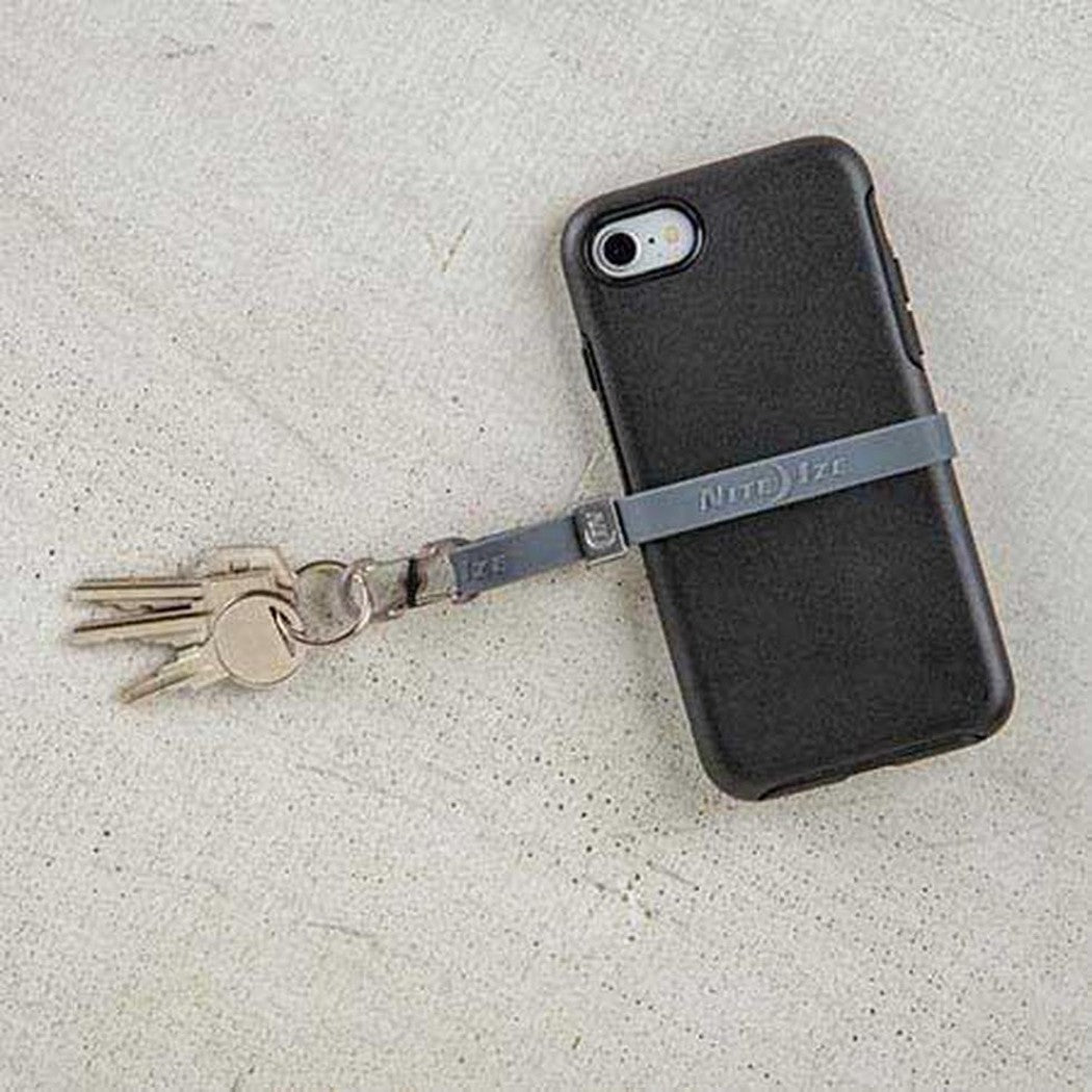 A black phone with a blue Nite Ize Cinch-A-Lot Stretch Strap and keys attached sits on a light gray surface.